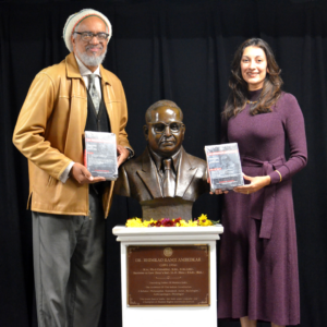 Dr. Amilcar Shabazz and Dr. Nandita Mani posing with volumes of B.R. Ambedkar's works and a bronze bust of Ambedkar.