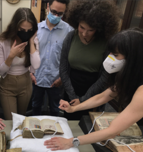 Students gather to look at an old book of psalms set on a white pillow on a table.